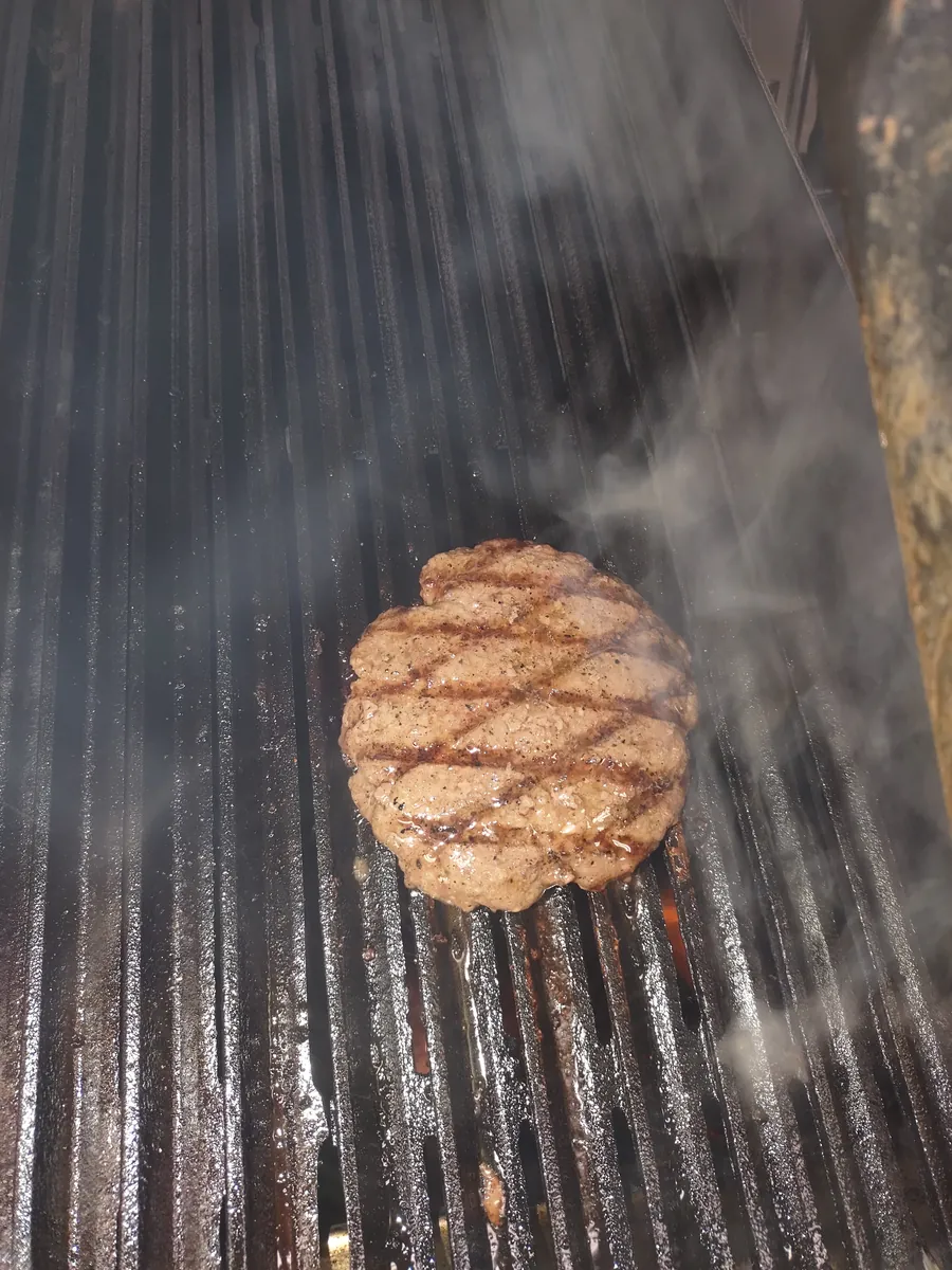 Hand-pattied burger smoking on the flat-top grill