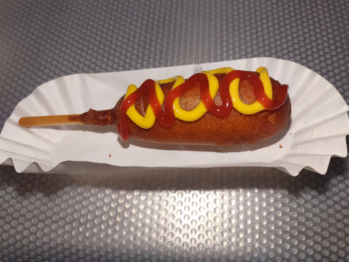 Golden corn dog drizzled with ketchup and mustard