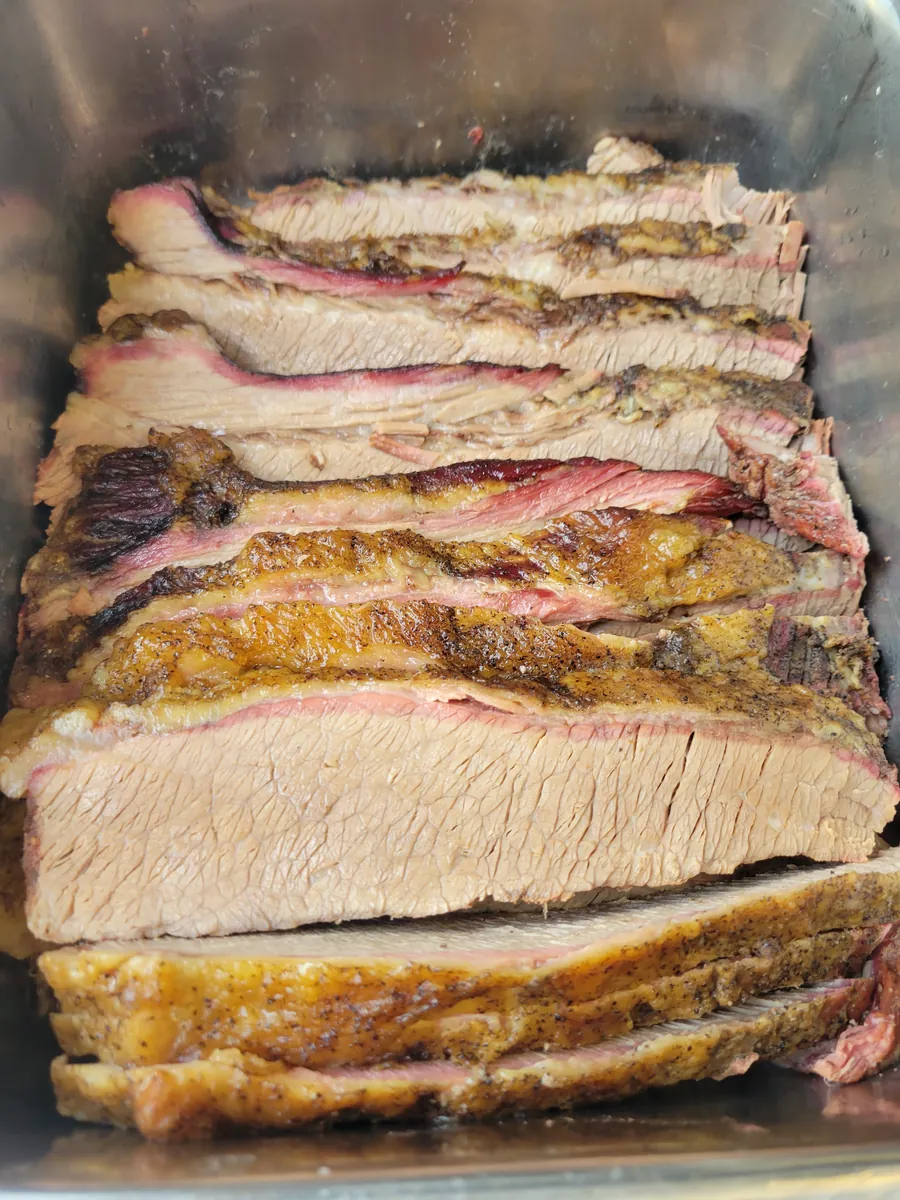 Slow-smoked brisket sliced and stacked in a serving pan